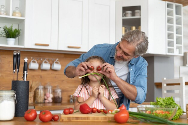 Cute little girl and her handsome dad are having fun while cooking in kitchen at home.