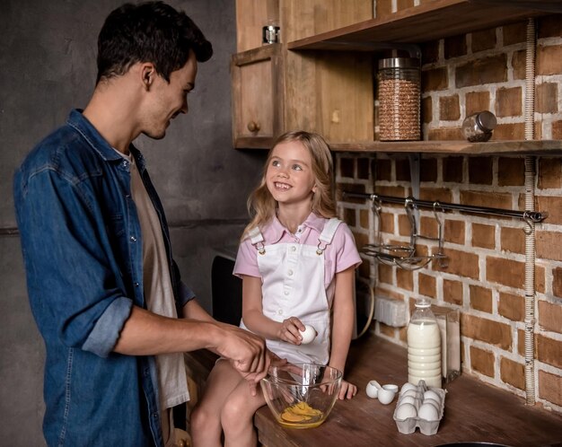 cute little girl and her handsome dad are smiling while cooking together in kitchen