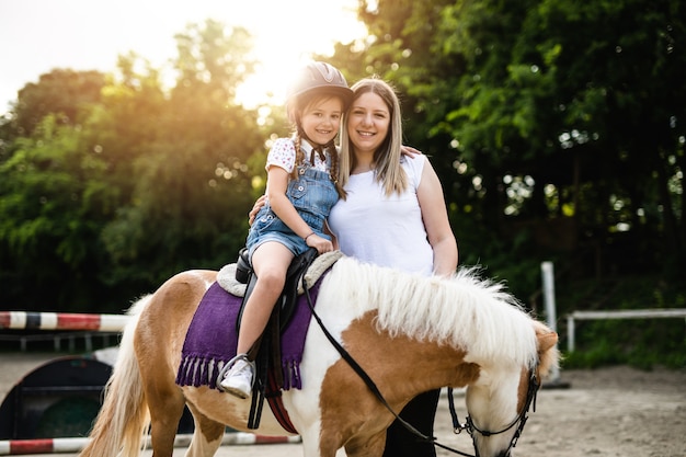 Photo cute little girl and her older sister enjoying with pony horse outdoors at ranch.