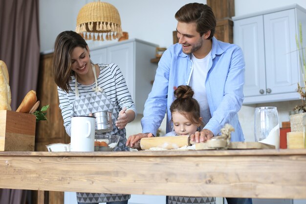 Cute little girl and her parents are having fun while cooking in kitchen at home together.