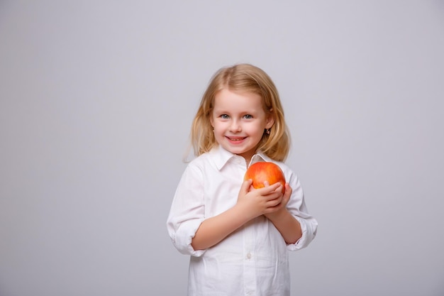 Bambina sveglia che tiene una mela su una priorità bassa bianca