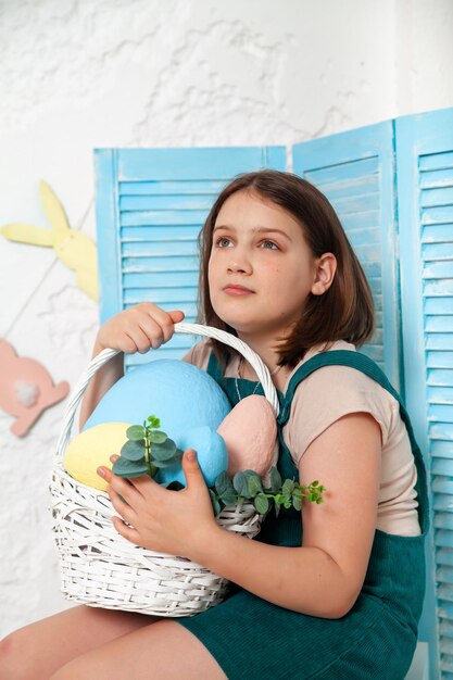 Cute little girl holding basket with Easter eggs and smiling with decoration in background