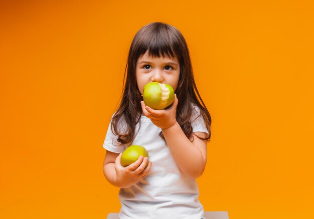 Photo cute little girl holding big green apples in her hands yellow isolated background healthy food for kids or healthy snack place for text