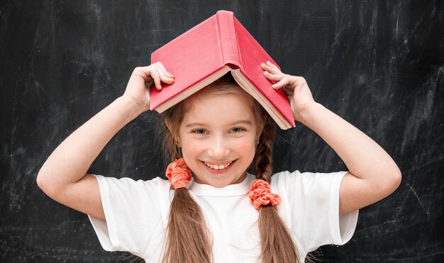 Bambina sveglia che tiene un libro sulla sua testa