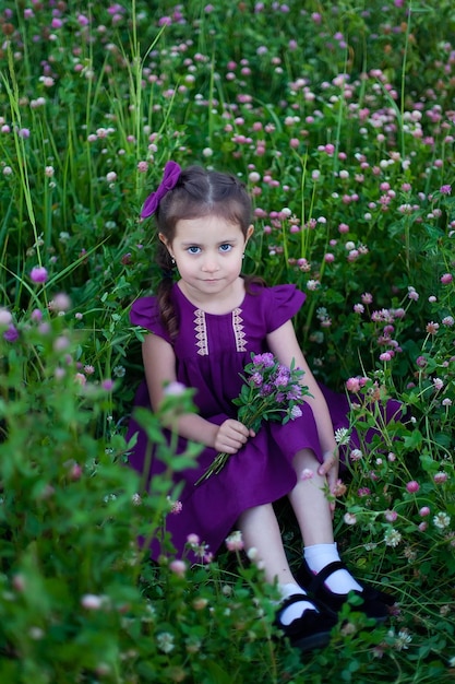 A cute little girl holding a bouquet of purple clover flowers in her hands a street portrait in the park summer walks