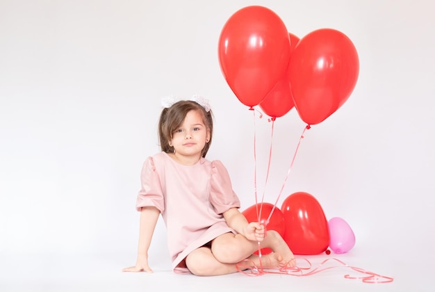 Bambina sveglia che tiene un mazzo di palloncini rossi a forma di cuore