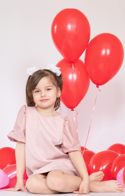 Bambina sveglia che tiene un mazzo di palloncini rossi a forma di cuore