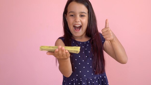 Cute little girl holding dollars, isolated over pink