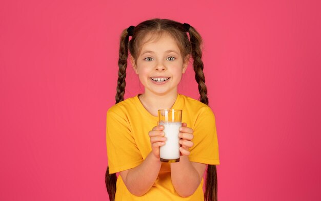 キュートな女の子がミルクのグラスを握ってカメラに微笑んでいる