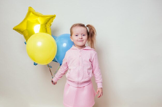 Cute little girl holding helium blue, yellow and gold balloons on white background in studio