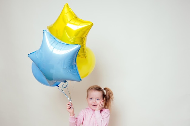 Cute little girl holding helium blue, yellow and gold balloons on white background in studio