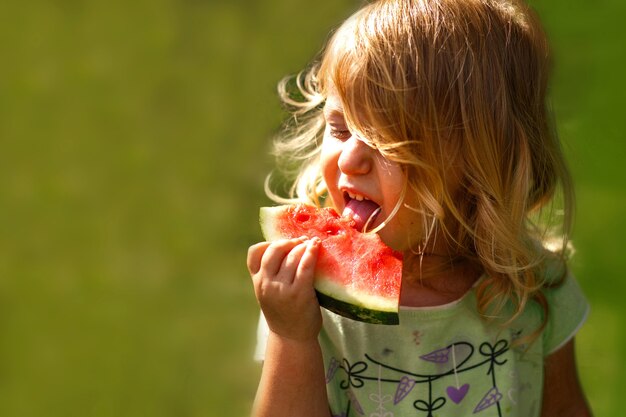 Cute little girl holding a piece of watermelon in the garden in summertime
