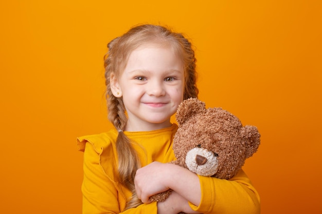 Cute little girl holding a teddy bear on a yellow background hugging