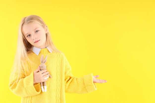 Cute little girl holds toy rabbit on yellow background