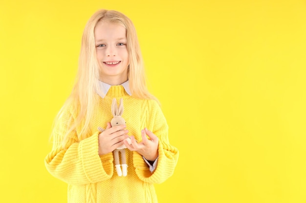 Cute little girl holds toy rabbit on yellow background