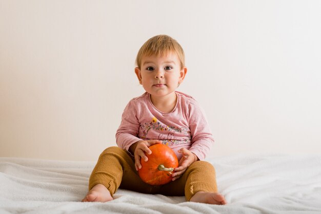 Bambina sveglia che abbraccia una zucca su un letto all'interno. copyspace