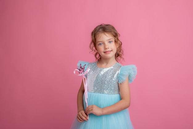Фото Милая маленькая девочка в красивом платье с волшебной палочкой на розовом фоне