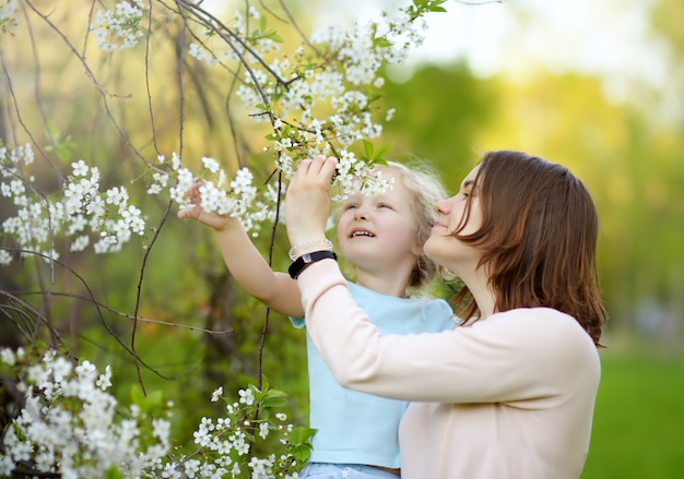 Милая маленькая девочка на руках своей красивой матери в вишневом или яблоневом саду во время цветения.