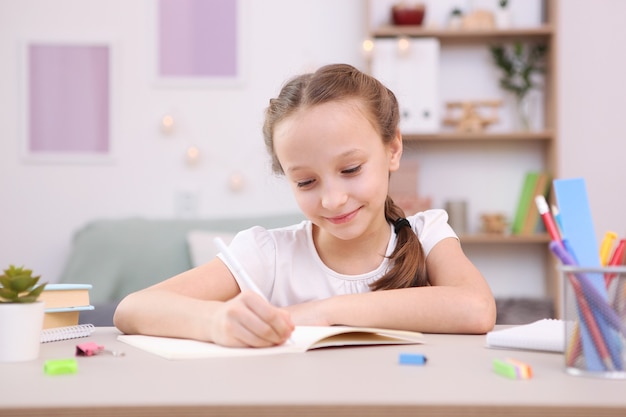 Cute little girl is doing homework in the interior of the room