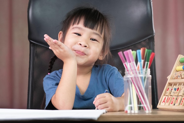 a cute little girl is drawing a rainbow on paper with colored pencils at the table at home