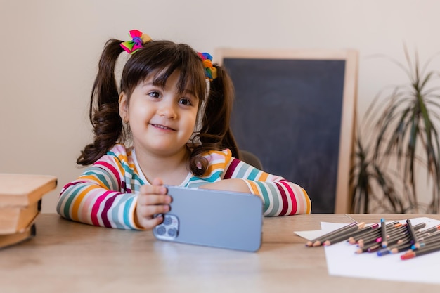 A cute little girl is engaged with a teacher online by phone Online education of children Preschoolers and gadgets