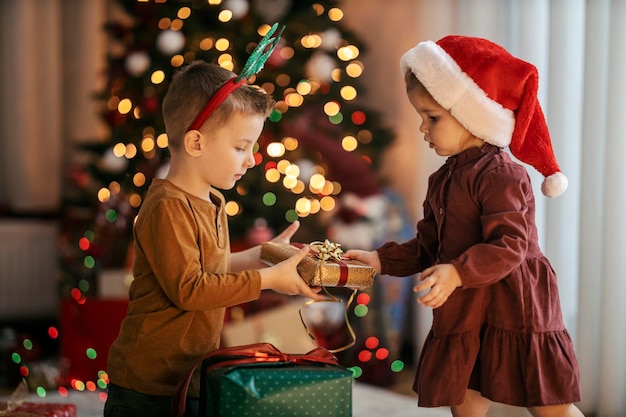 Cute little girl is giving a christmas gift to her big brother on christmas and new year