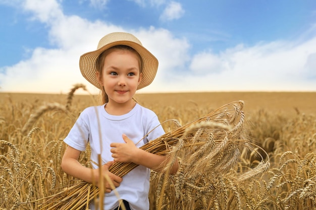 Cute little girl is holding golden ears of rye on walking on wheat field