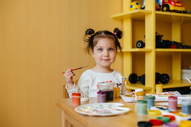 Милая маленькая девочка играет и рисует в своей комнате