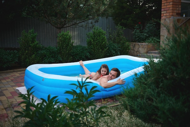 Cute little girl is playing water games with her loving father\
in the inflatable pool in the backyard garden at home