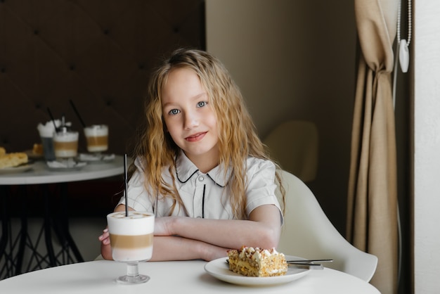 かわいい女の子がカフェに座って、ケーキとココアのクローズアップを見ています。食事と適切な栄養。