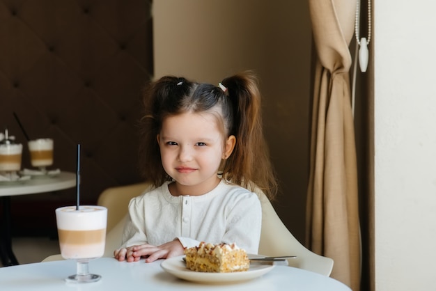 Una bambina carina è seduta in un caffè e guarda una torta e un primo piano di cacao. dieta e corretta alimentazione.