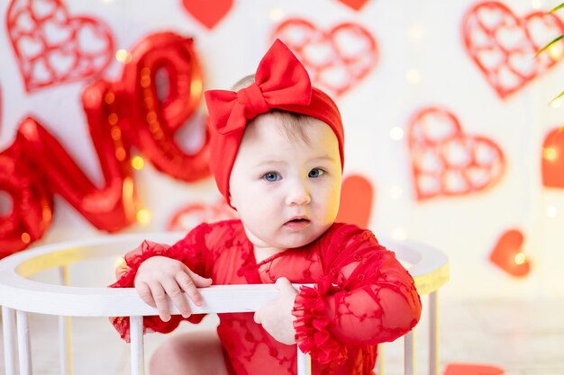 a cute little girl is sitting in a red bodysuit against a background of red hearts and the inscription love. the concept of valentine's day, valentine's day