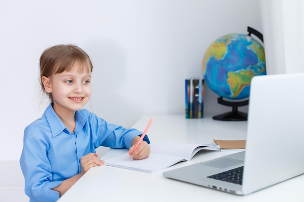 Cute little girl is sitting at table with her laptop and studying online