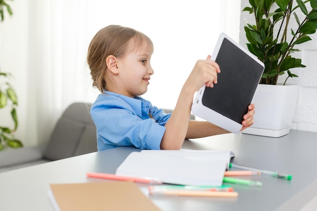 Cute little girl is sitting at table with her laptop and studying online