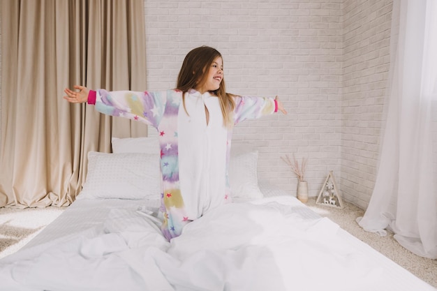 A cute little girl is stretching in bed in her bedroom on white linens.