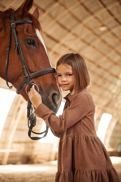 Photo cute little girl is with horse indoors