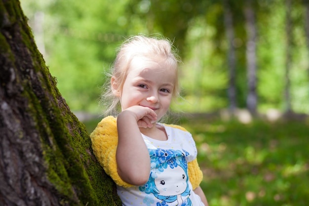 Cute little girl in knitted yellow bolero posing at a tree