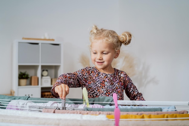 Cute little girl in the laundry room clean washed clothes on drying rack mothers helper sweet child