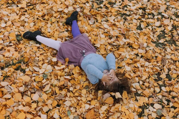 写真 秋の時間に公園で黄色の葉の上に横たわっているかわいい女の子秋のカードバナー健康