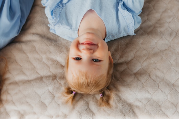 Cute little girl lies on the bed and smiles. view from above. portrait of a child