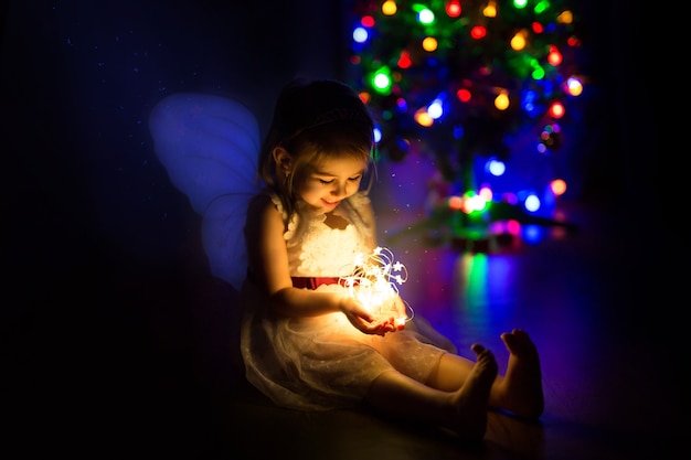 A cute little girl lights a Christmas garland a magical holiday