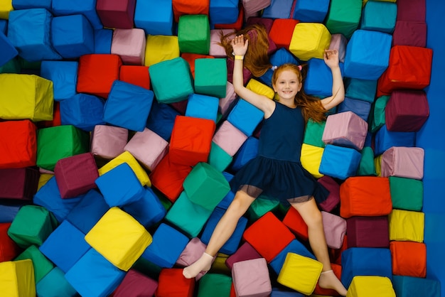 Cute little girl lying in soft cubes, playground in entertainment center.