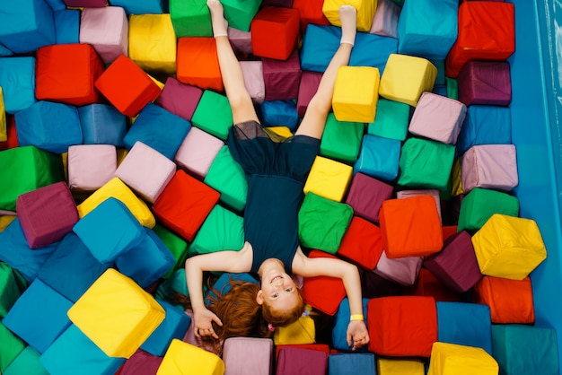 Cute little girl lying in soft cubes, playground