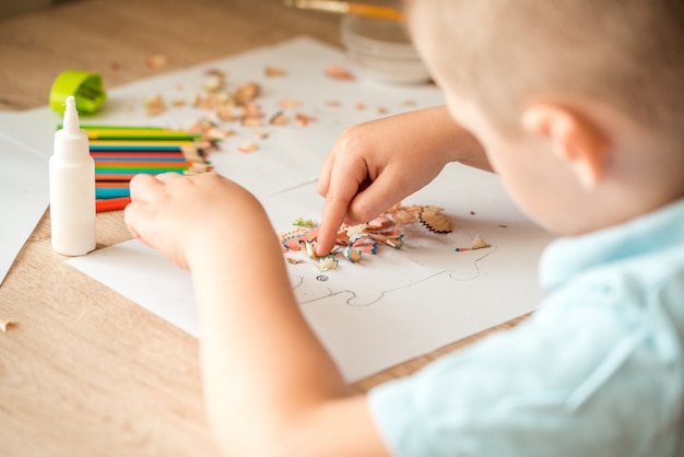 Cute little girl make applique glues colorful house, applying color paper using glue while doing arts and crafts in preschool or home. Idea for children's creativity, an art project made of paper.