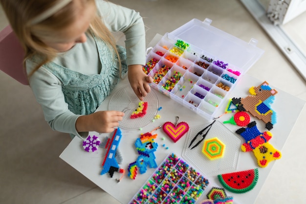 Милая маленькая девочка делает игрушку с термо мозаикой