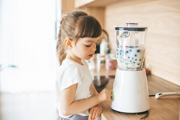 Cute little girl making a delicious fruit smoothie with a blender