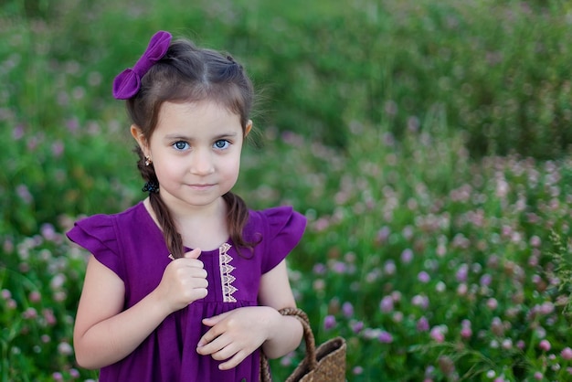 여름날 초원에 있는 귀여운 소녀가 보라색 클로버 꽃다발을 수집하고 있다