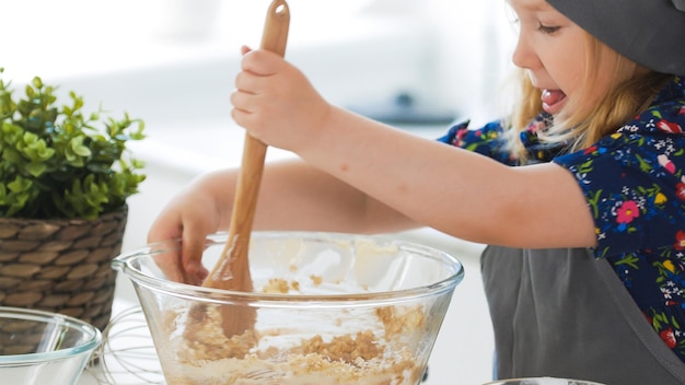 Cute little girl mixing the dough for cookies with wooden spoon in glass bowl horizontal