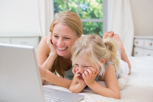 Cute little girl and mother on bed using laptop