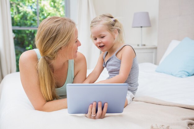 かわいい女の子とお母さん、ベッドを使ってタブレット